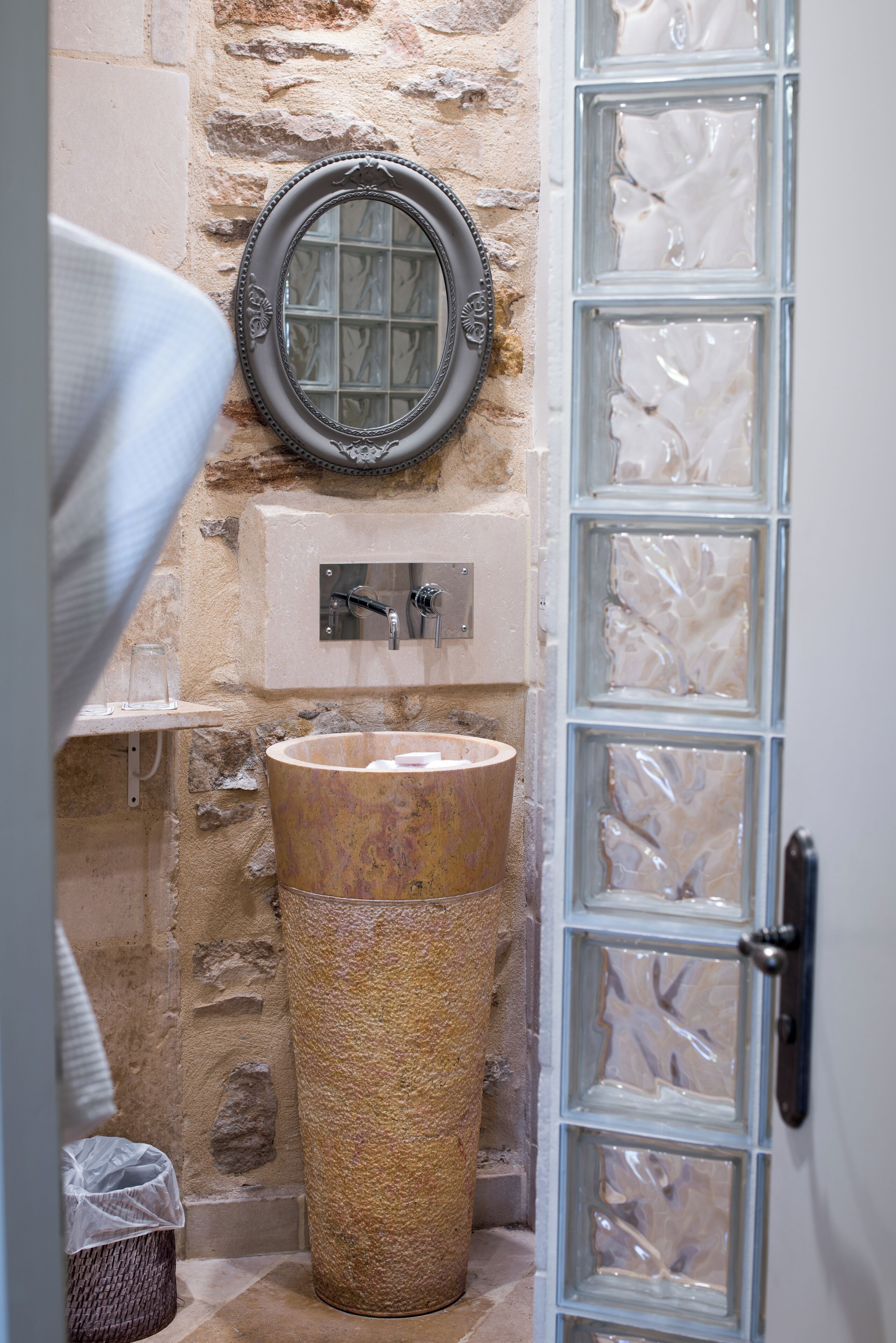 A bathroom with a stone wall, a wooden basin, a mirror, and a glass door.