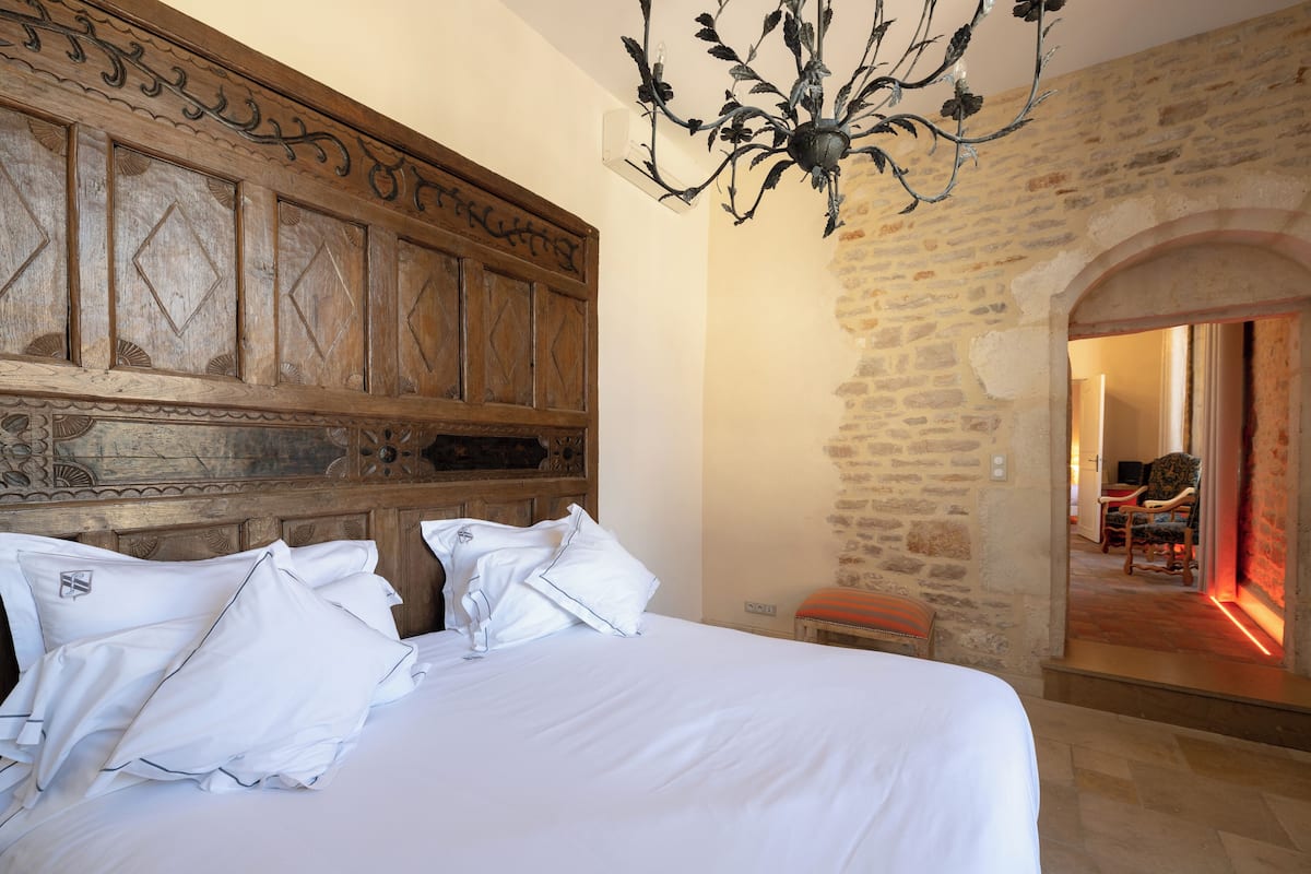Een slaapkamer met een groot bed, houten hoofdeinde en een kroonluchter.