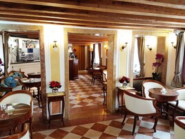 A hotel lobby with checkered flooring, wooden furniture, and a coffee machine in the background.
