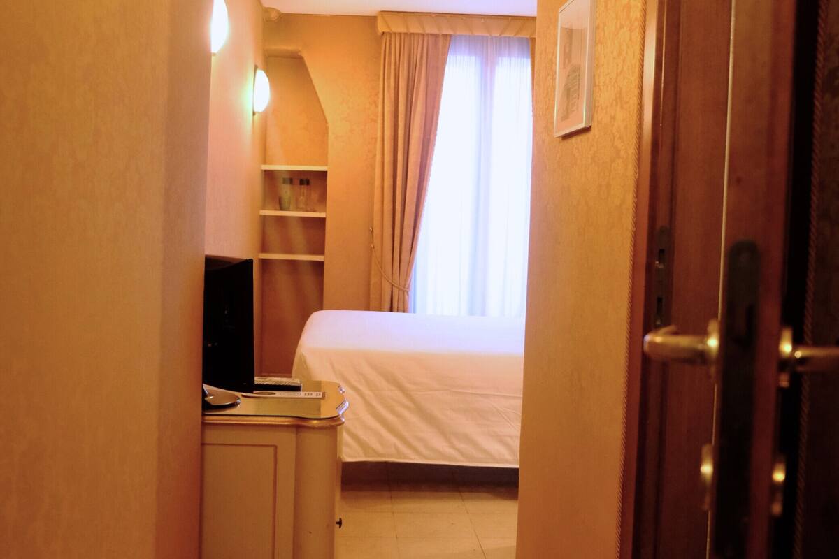 A narrow hotel corridor with a bed, a desk, and a television.