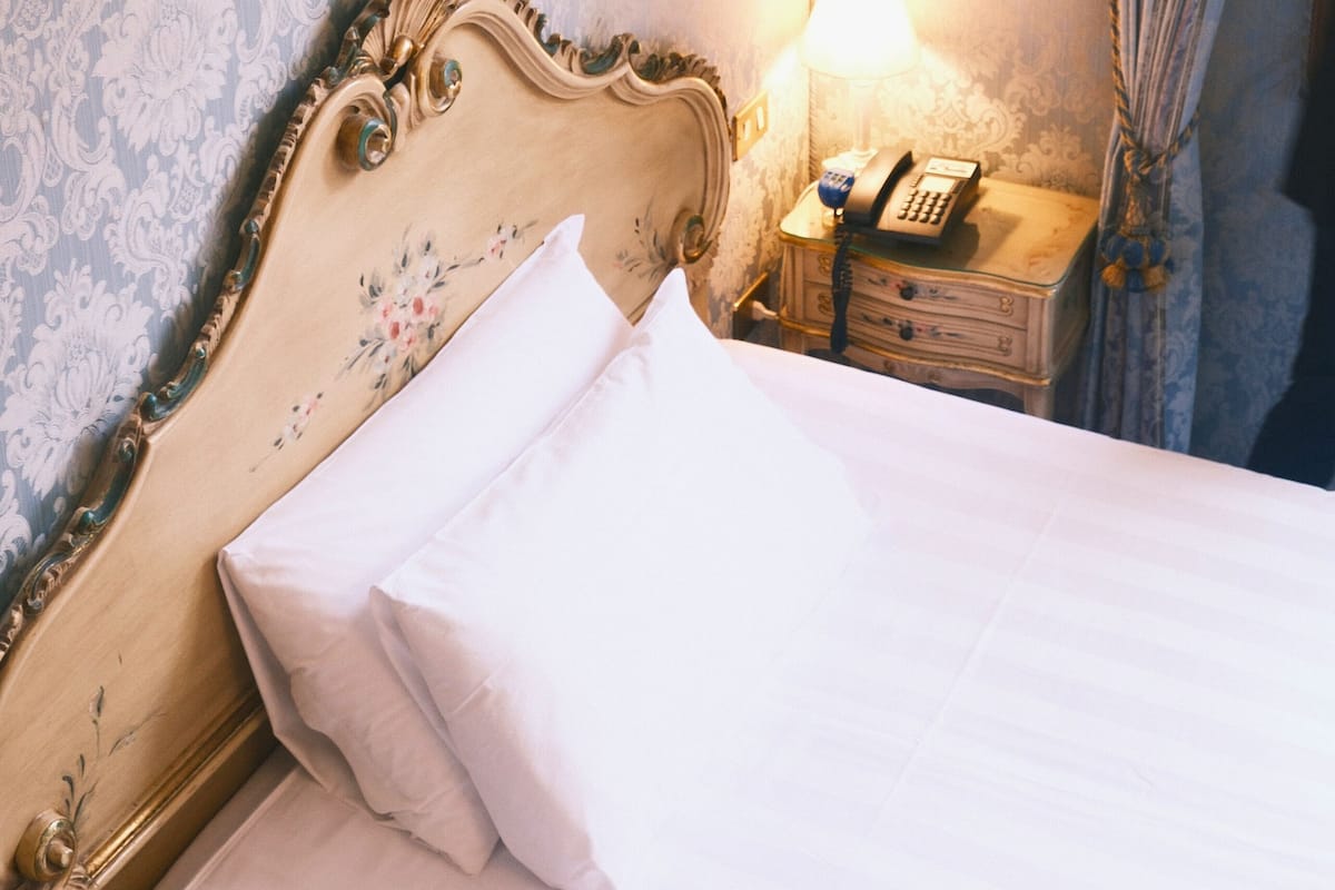 A bed with a floral headboard, a bedside lamp, and a nightstand with a telephone.