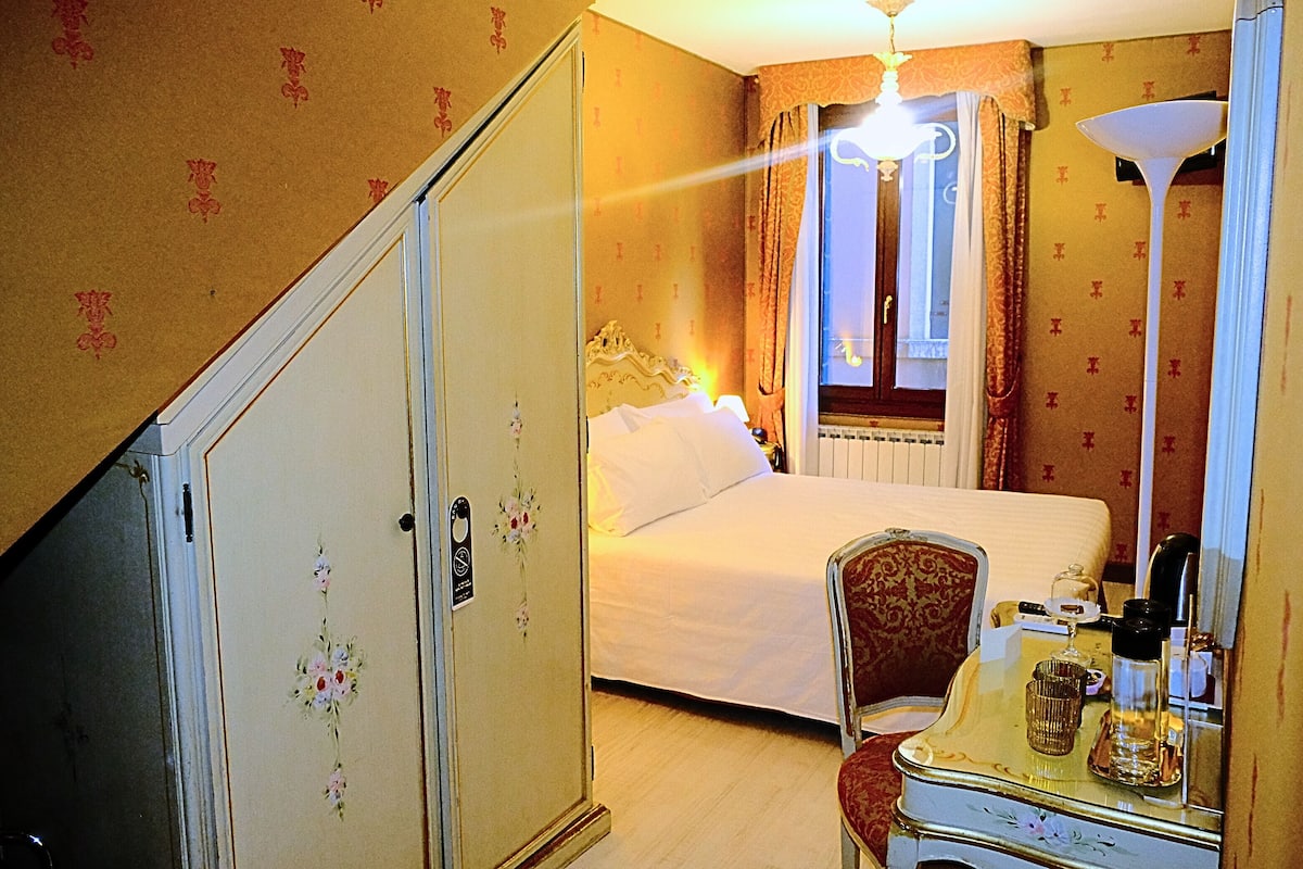 A hotel room with a bed, a chair, a table with a lamp, and a mirror.