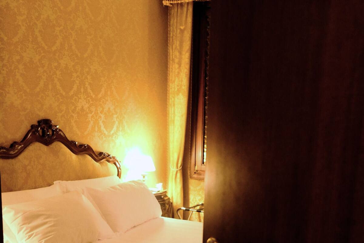 A hotel room with a bed, a nightstand, and a lamp.