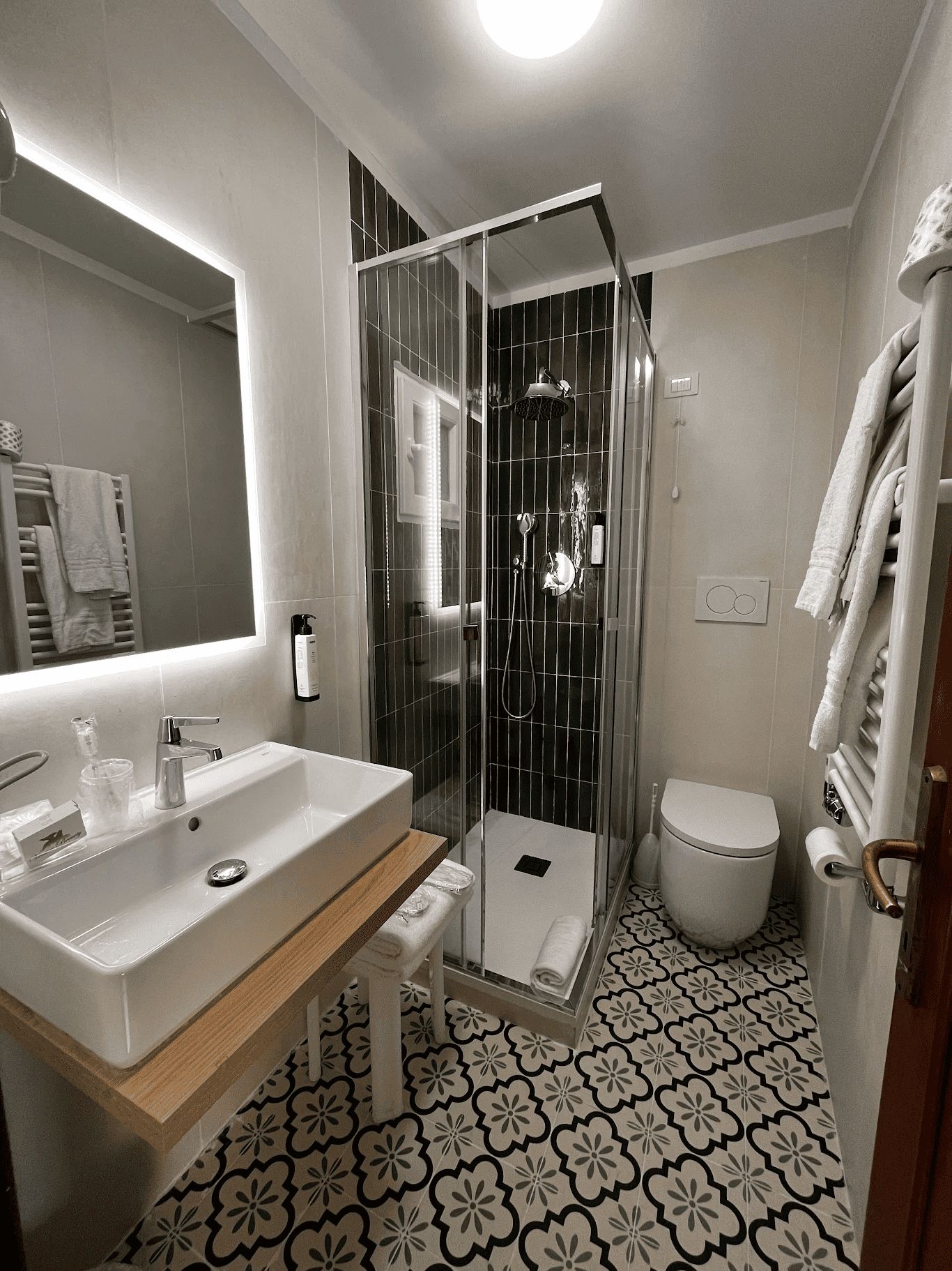 Een moderne badkamer met een douchecabine van glas, een wit wastafeltje en een toilet.