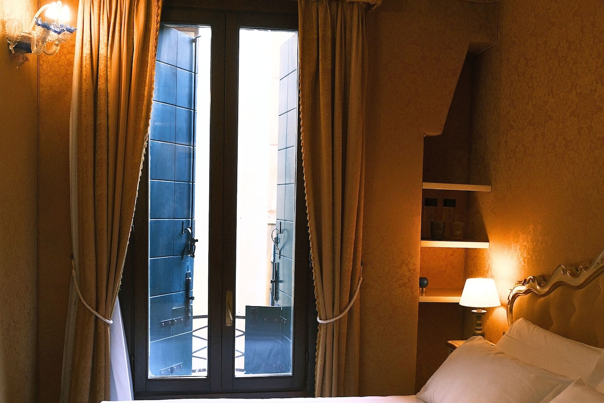A hotel room with a bed, curtains, a window, a nightstand, and a lamp.