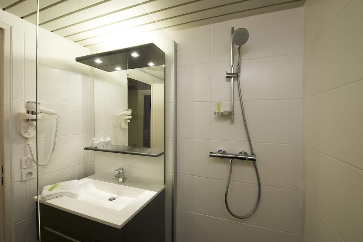 Une salle de bain moderne avec un lavabo blanc, un miroir, une douchette à main et une douche à parois de verre.