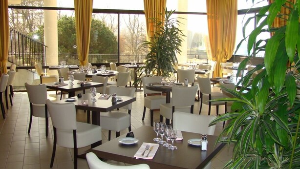 Um restaurante com várias mesas, cadeiras e uma grande janela com cortinas.