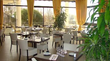 A restaurant with multiple tables, chairs, and a large window with curtains.