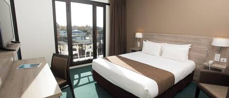 A hotel room with a bed, desk, chair, and a large window with a view.