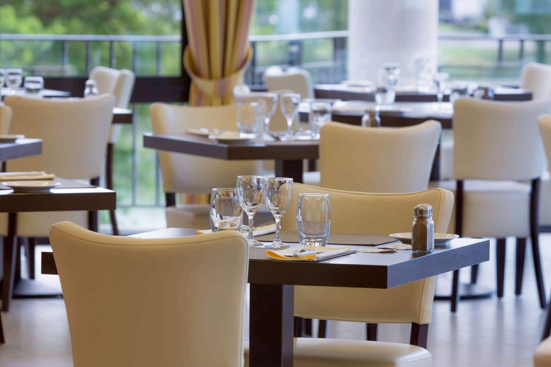 Un restaurante con mesas dispuestas para comer, sillas y vistas al exterior con vegetación.