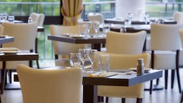 Un restaurante con mesas dispuestas para comer, sillas y vistas al exterior con vegetación.