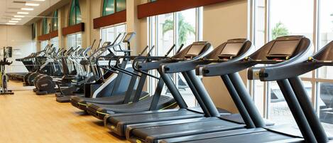 Varias cintas de correr en un gimnasio con amplios ventanales y suelo de madera.