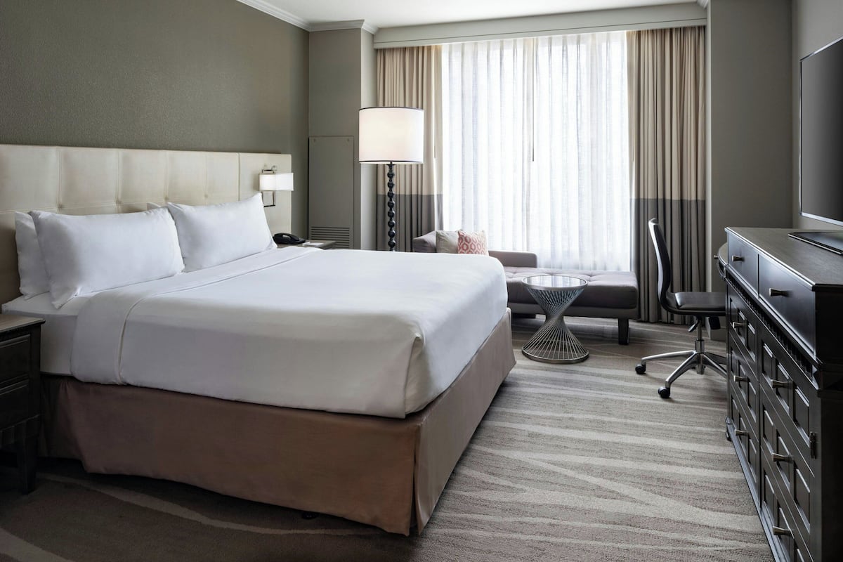 Een hotelkamer met een groot bed, een bureau, een stoel, een televisie en een raam met gordijnen.