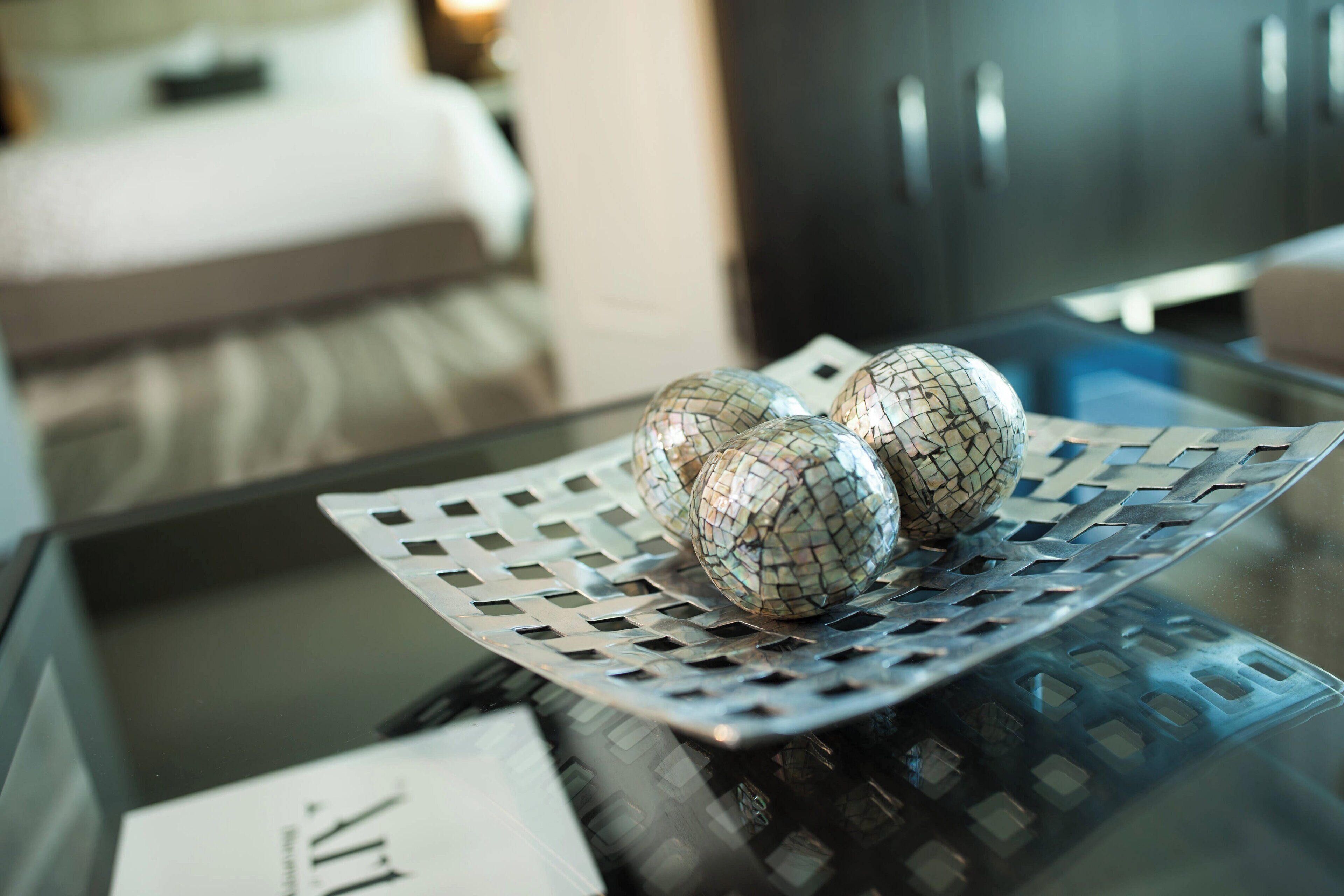 A glass table with a decorative metal tray holding three spherical objects.