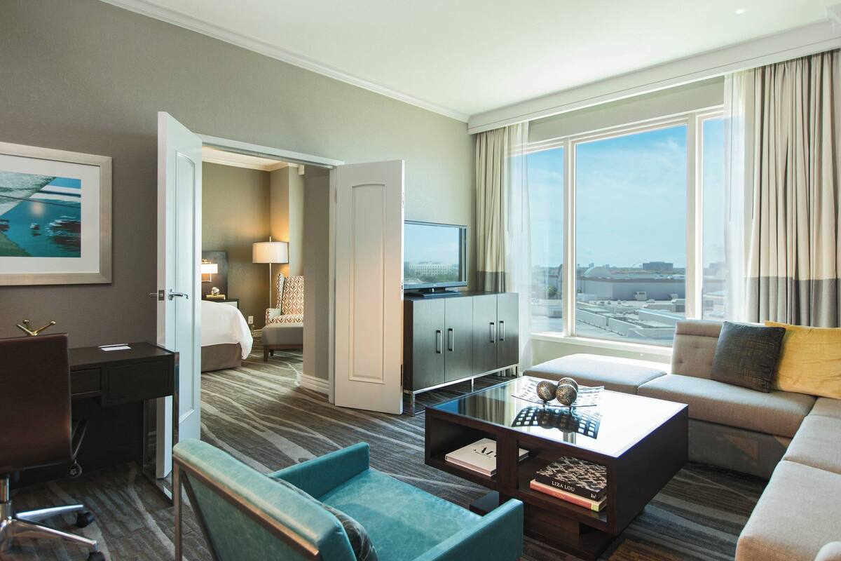 Een hotelkamer met een bed, een bureau, een televisie, een bank en uitzicht op de stad.