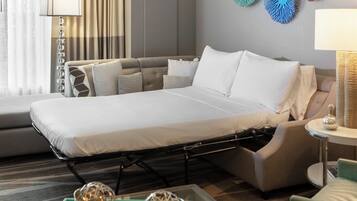A hotel room with a bed, a sofa, a side table, and decorative wall art.