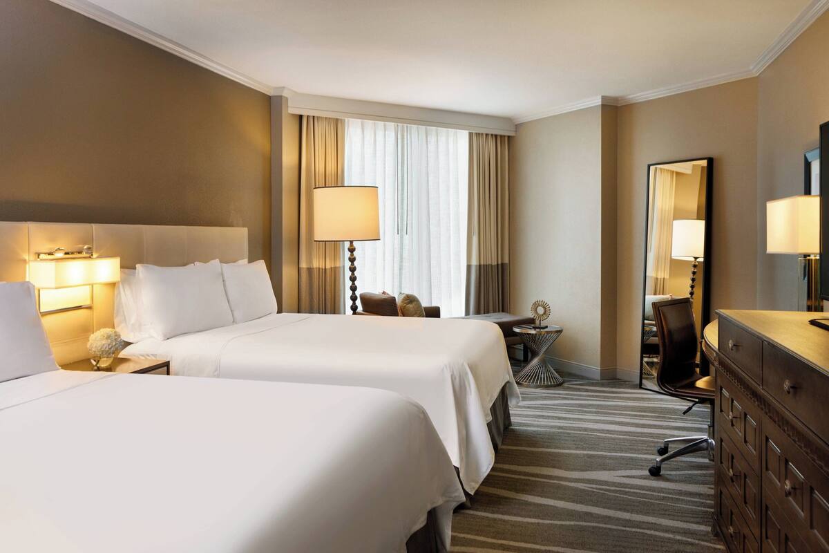 Een hotelkamer met twee bedden, een bureau, een stoel, een kledingkast en een grote spiegel.