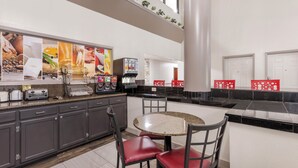 A modern kitchen with granite countertops, a round dining table, and red chairs. - Red Roof Inn & Suites Clinton, MS (Clinton)