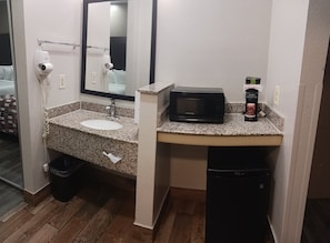Un baño con lavamanos de granito, secador de pelo, microondas y un bote de basura.