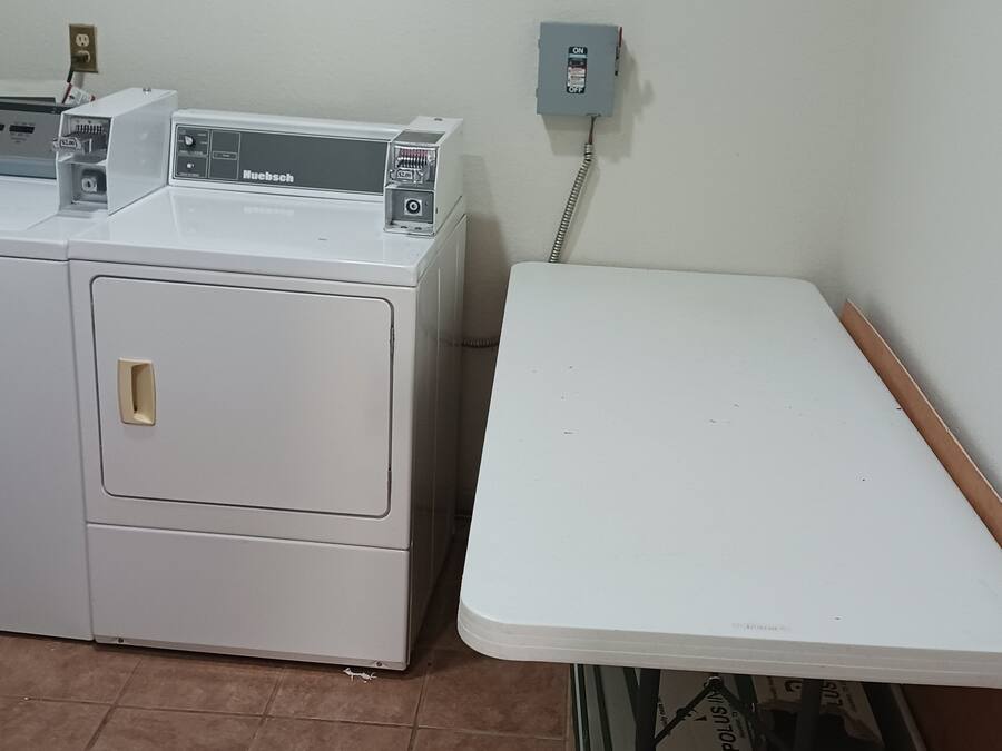 A compact, white, two-door laundry machine with a control panel and a power outlet on the wall.