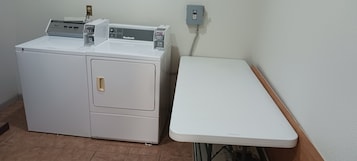 Una lavadora blanca y compacta, de dos puertas, con un panel de control y un enchufe en la pared.