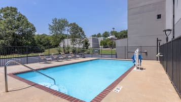 A rectangular swimming pool with a metal ladder, surrounded by a brick border and a black fence.
