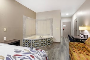 Habitación de hotel con una bañera grande, una cama con colcha estampada, una silla y un escritorio con lámpara.