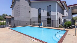 A swimming pool with a metal ladder and a safety sign, surrounded by a concrete deck and a metal fence. - Red Roof Inn & Suites Clinton, MS (Clinton)