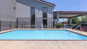 A swimming pool with a covered area, a building with a red roof, and a fenced perimeter.