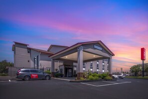 A hotel with a covered entrance, a parking lot, and a sunset sky. - Red Roof Inn & Suites Clinton, MS (Clinton)