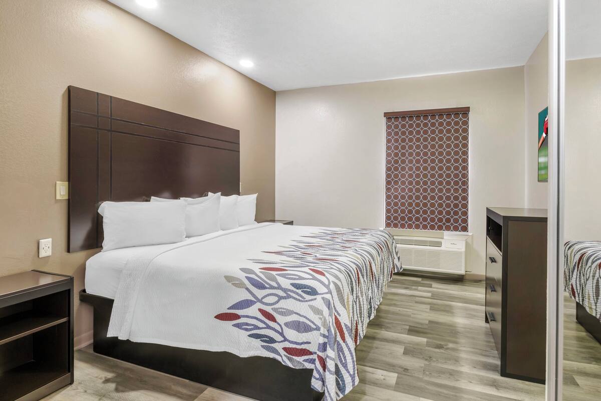 A hotel room with a large bed, a bedside table, a wardrobe, and a window with a decorative screen.