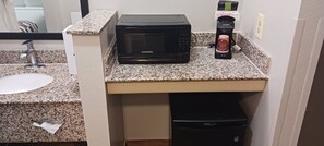 A kitchen area with a microwave, coffee maker, sink, and a trash bin.