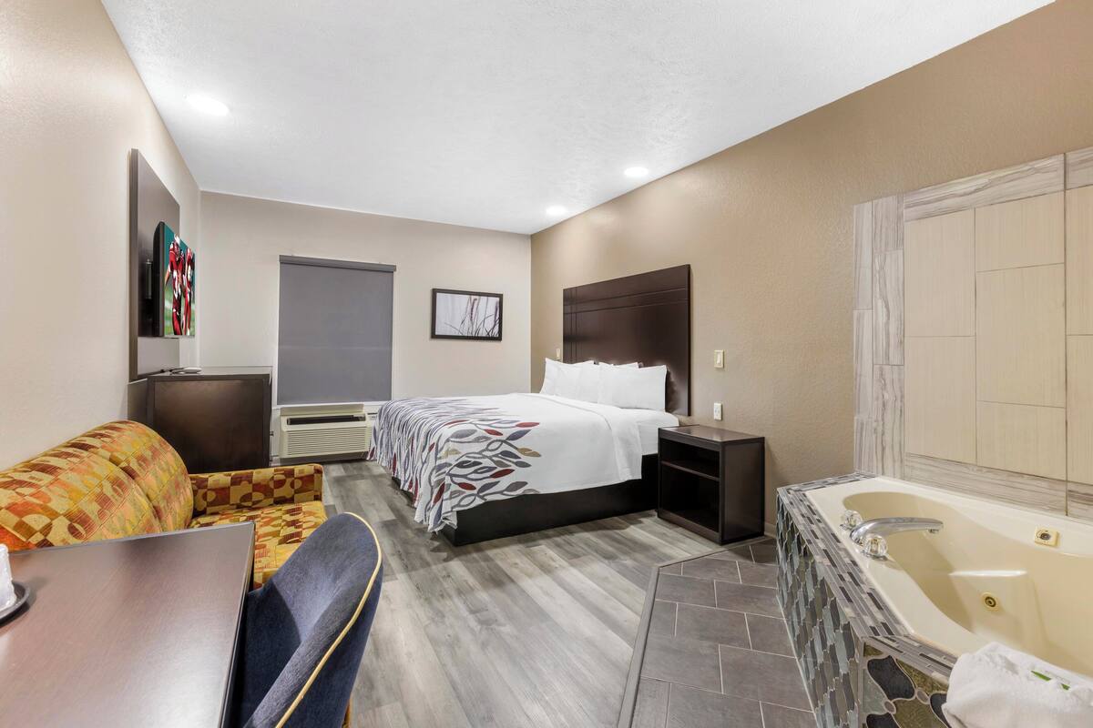 A hotel room with a bed, a sofa, a desk, a bathroom with a bathtub, and a TV.