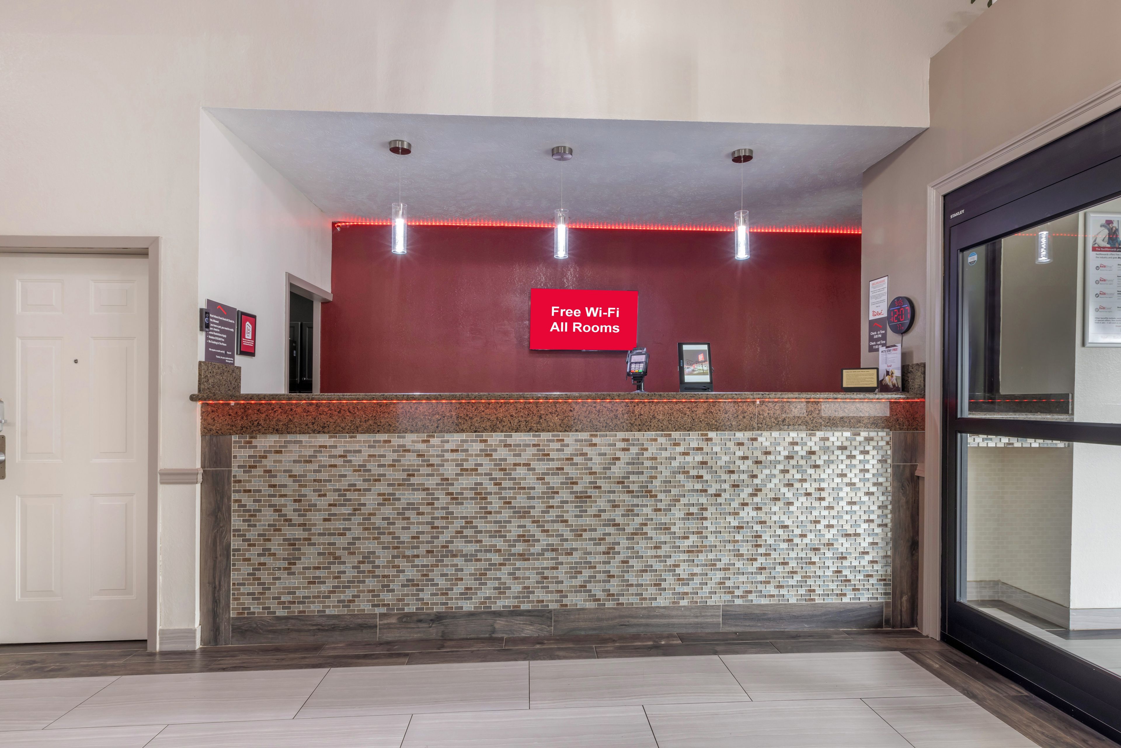 A reception area with a red wall, a mosaic tile wall, and a sign stating "Free Wi-Fi All Rooms."