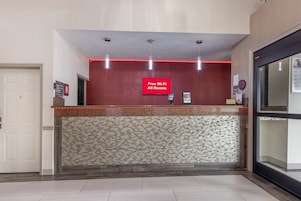 Un área de recepción con pared roja, pared de mosaicos y un cartel que indica 'Wi-Fi gratuito en todas las habitaciones'.