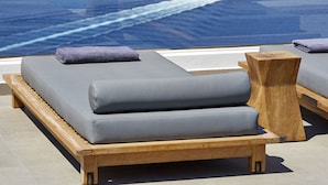 A sun lounger with a view of the ocean and a boat in the distance. - Volcano View Hotel Santorini (Santorini)