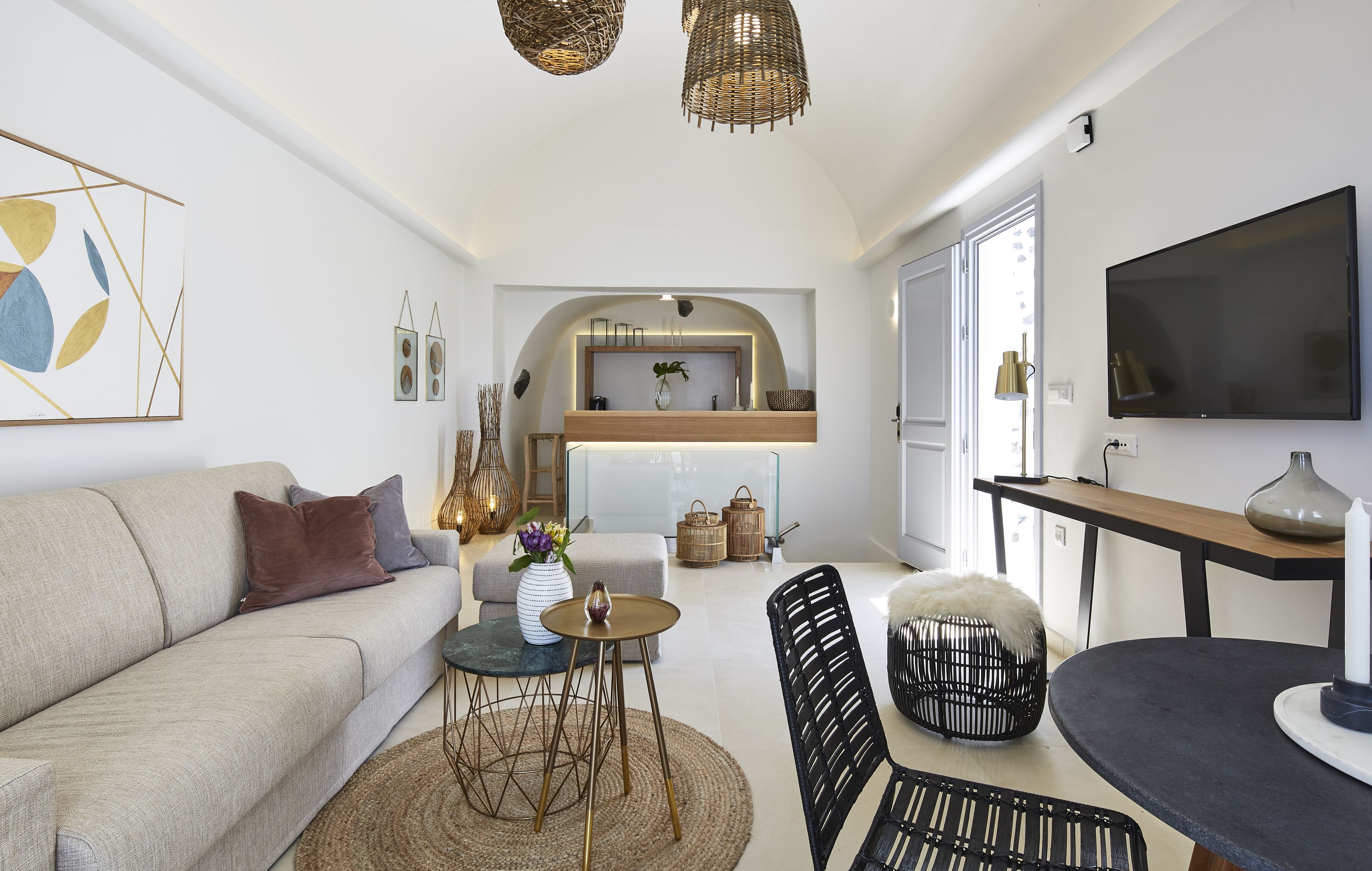 A modern living room with a sofa, coffee table, and chairs, a kitchen area with a TV, and a dining table with a candle.