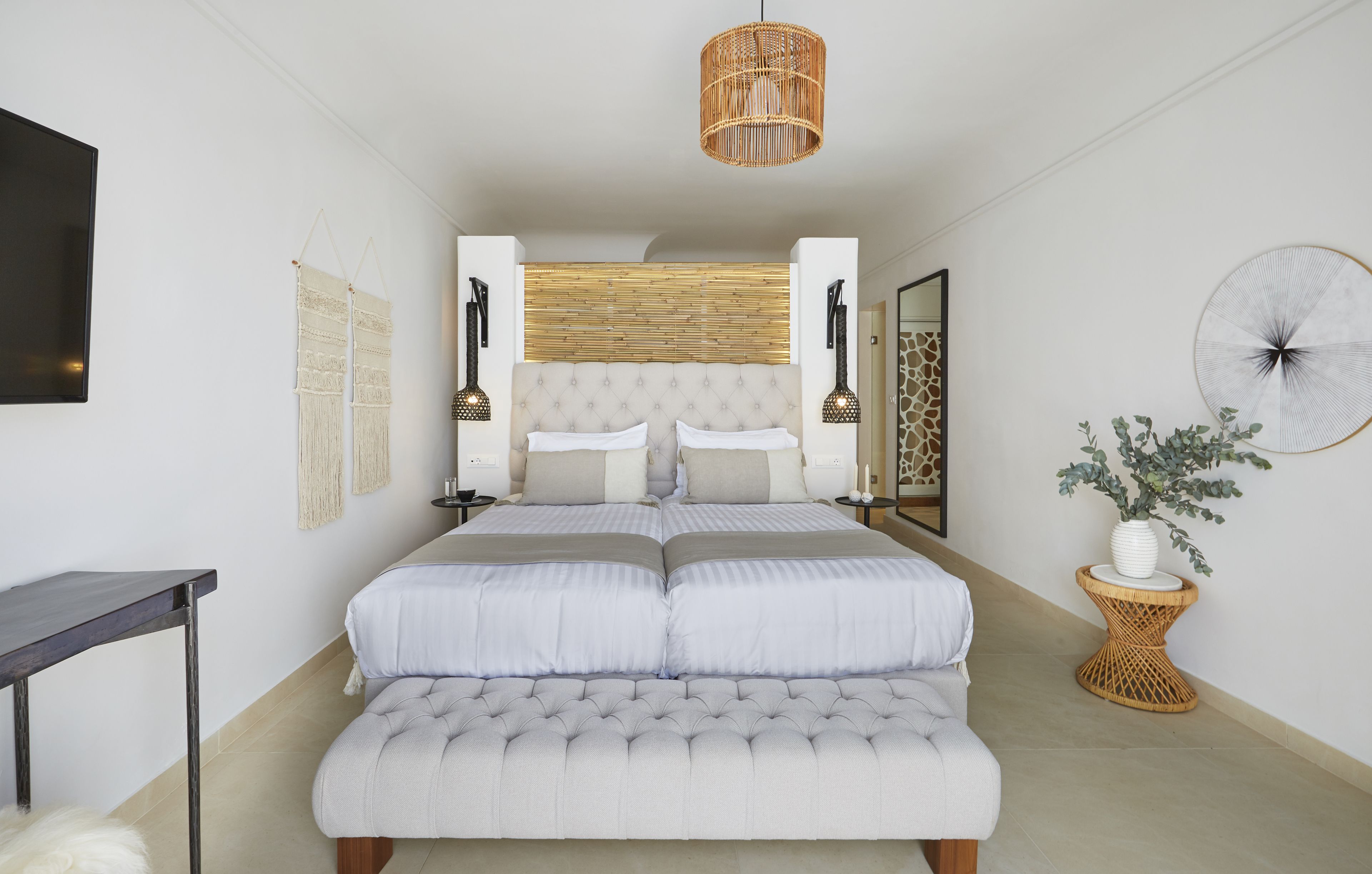 A bedroom with a large bed, bedside tables, a hanging light fixture, and a potted plant.