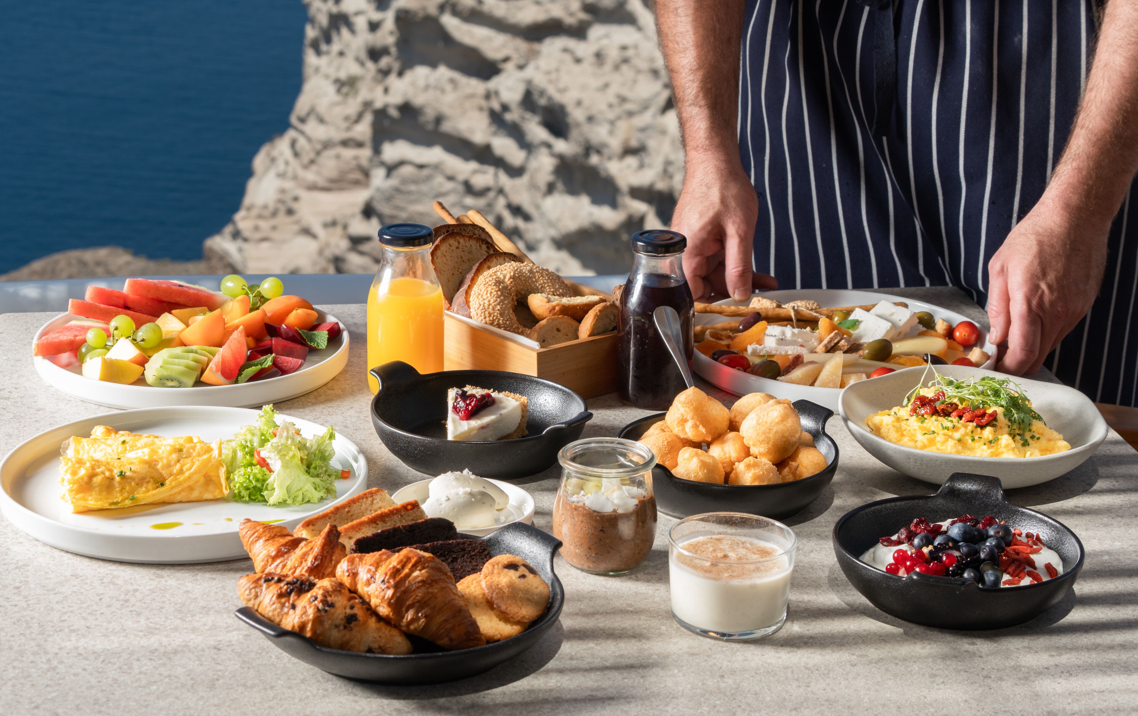 A breakfast spread with various dishes and a scenic beach view in the background.