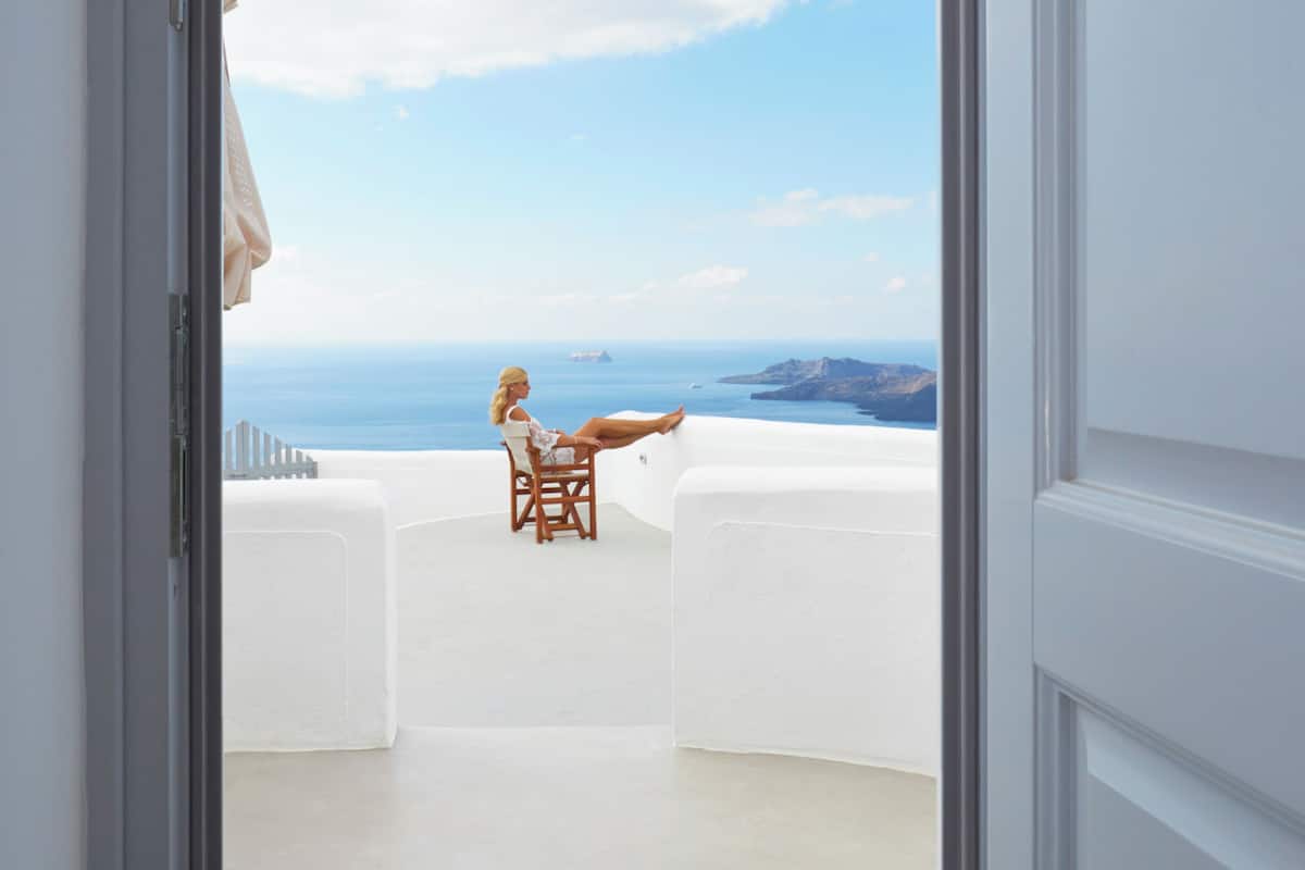A balcony with a white interior, a wooden chair, and a view of the sea and distant land.