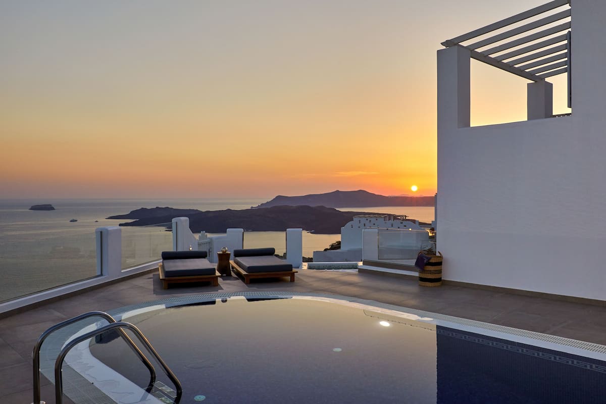 A rooftop infinity pool with lounge chairs and a view of the sunset over the sea.