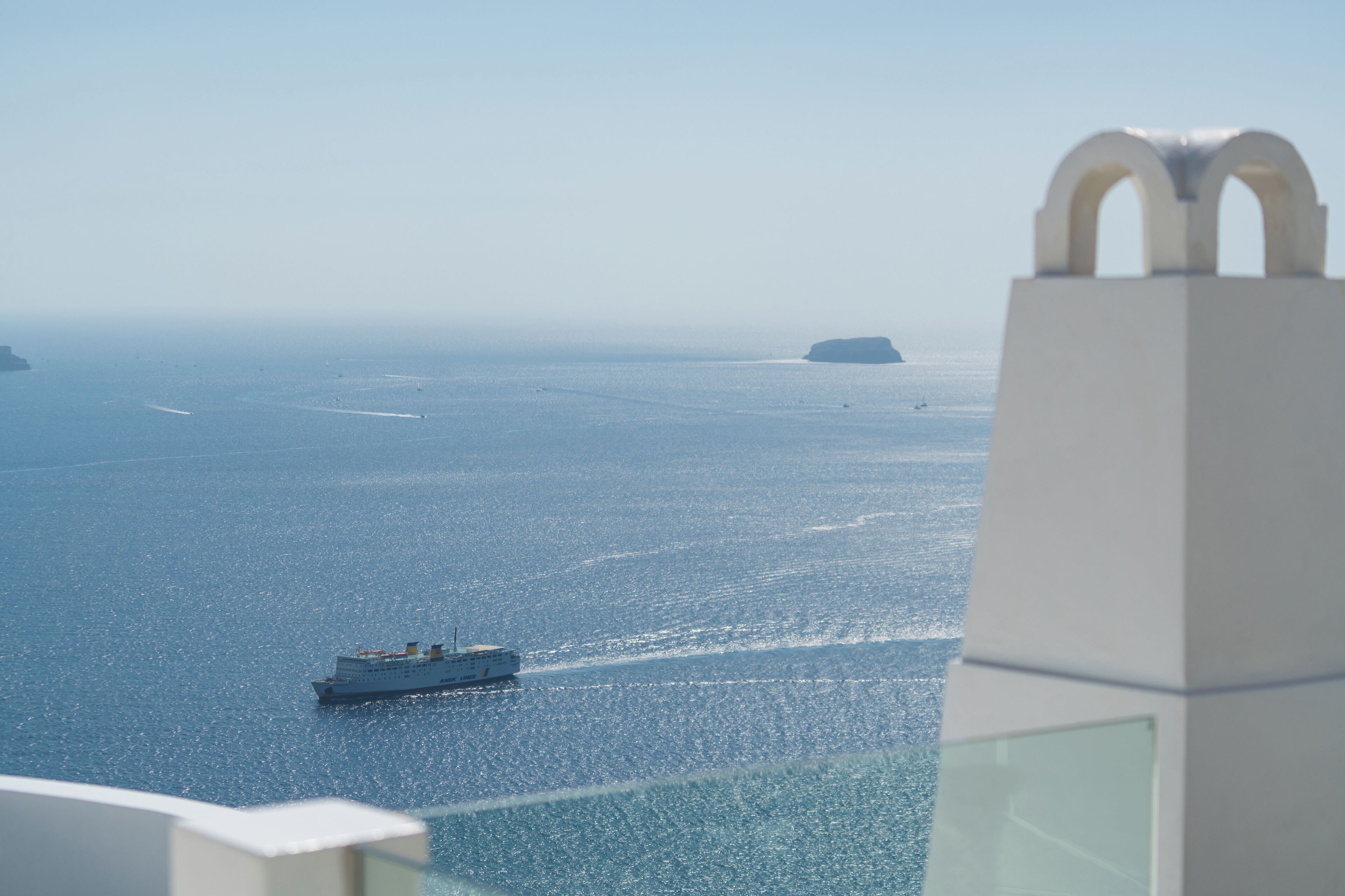 A view of a calm sea with a ship in the distance and a white building with a distinctive arched top in the foreground.