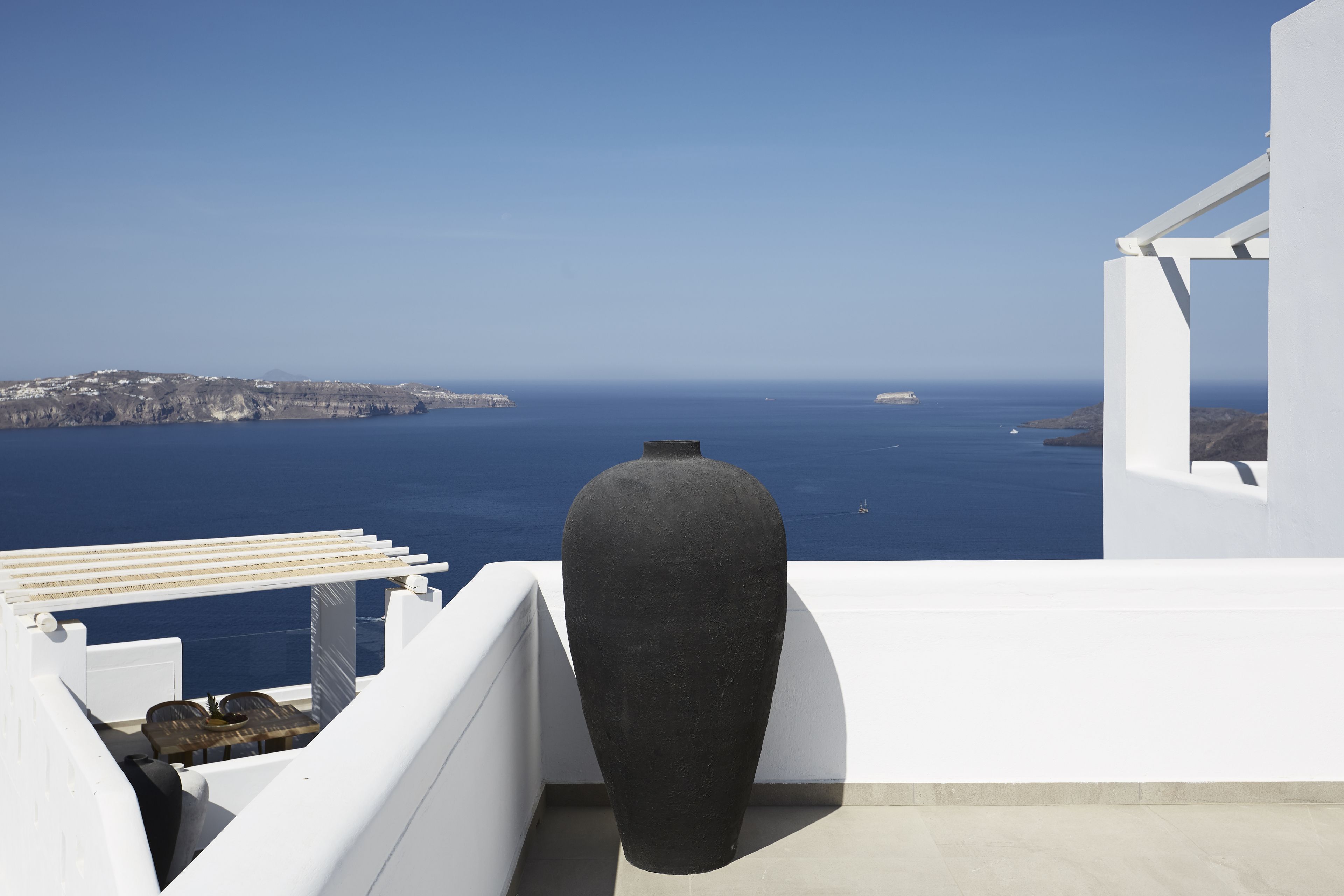 Un balcón blanco con un jarrón negro grande y vista al mar y la costa lejana.