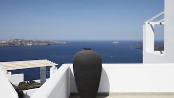 Un balcón blanco con un jarrón negro grande y vista al mar y la costa lejana.