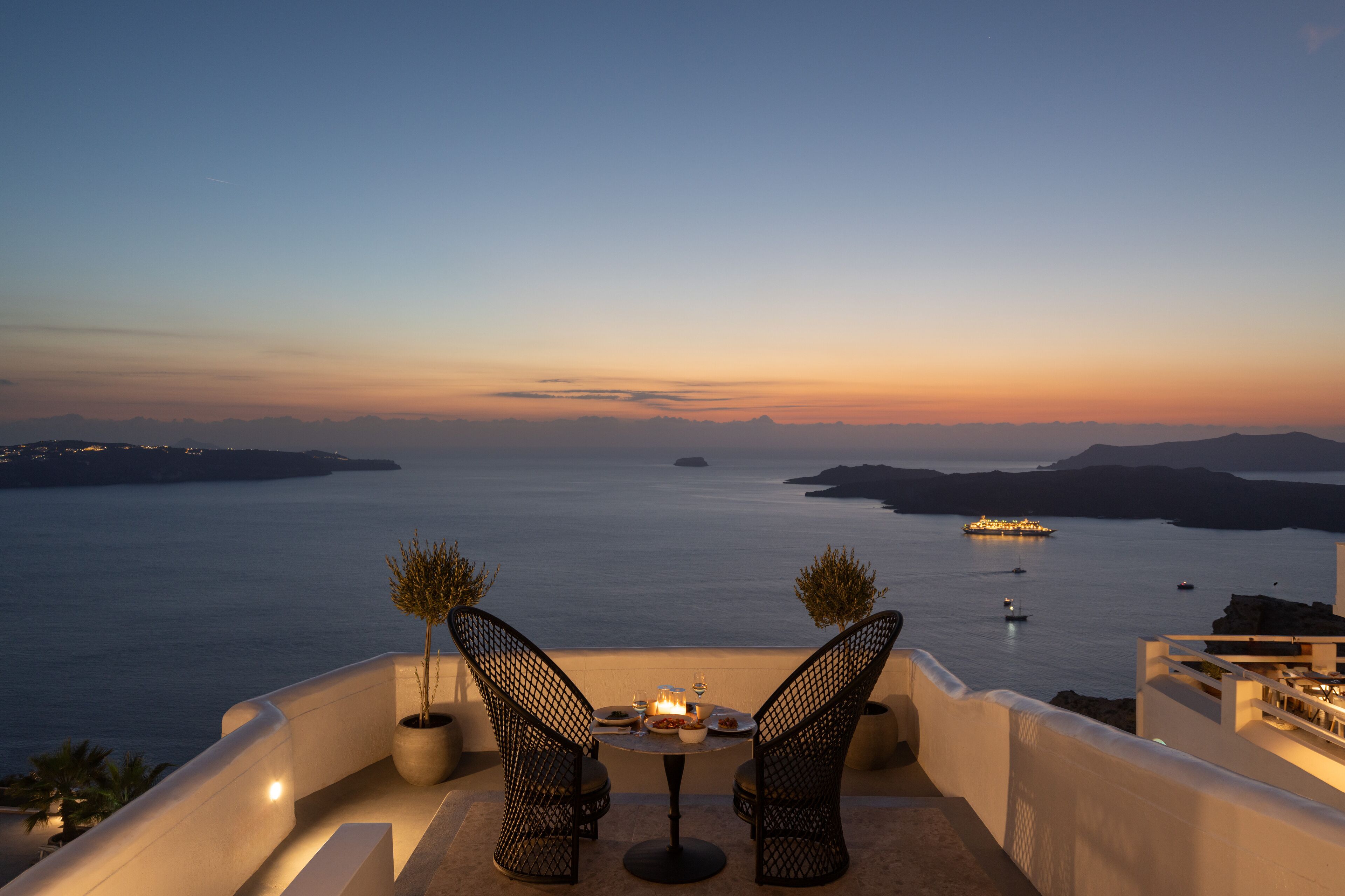 Une terrasse avec deux chaises et une table, donnant sur une étendue d’eau où l’on peut apercevoir des bateaux et, au loin, des reliefs terrestres.