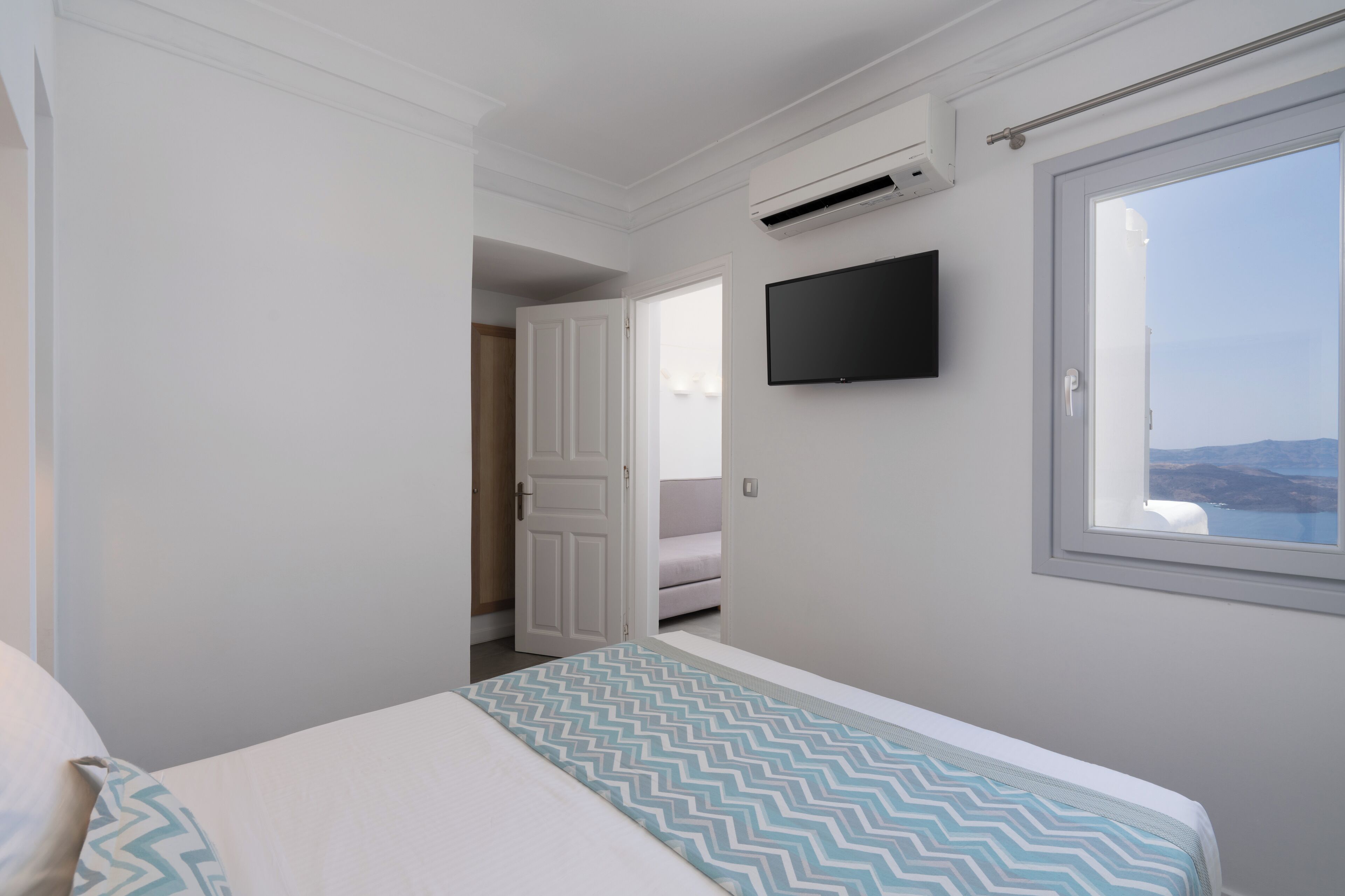 Habitación de hotel con cama, televisor montado en la pared y ventana con vistas.