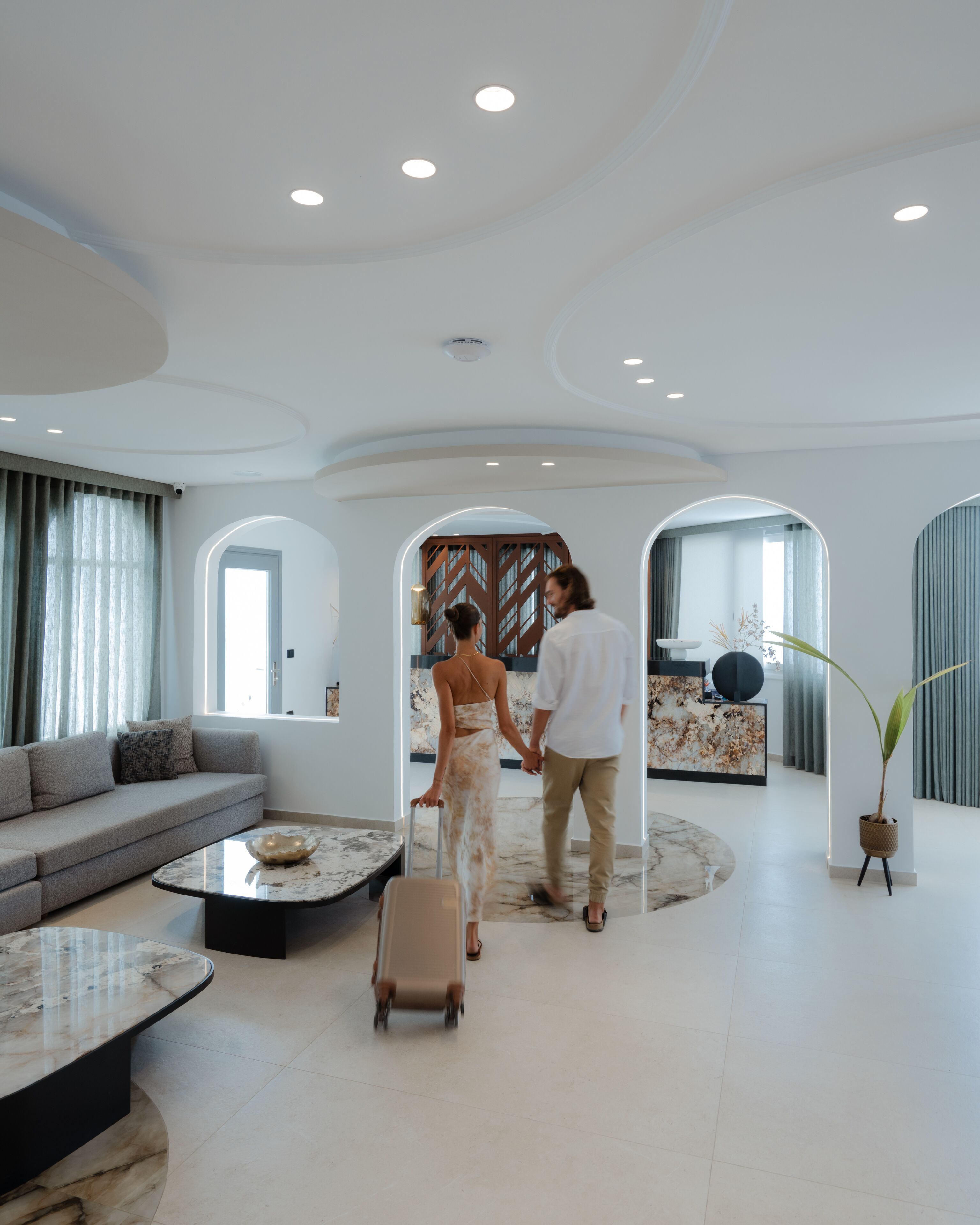 A spacious, modern hotel lobby with a curved ceiling, a reception desk, a seating area, and a large plant.
