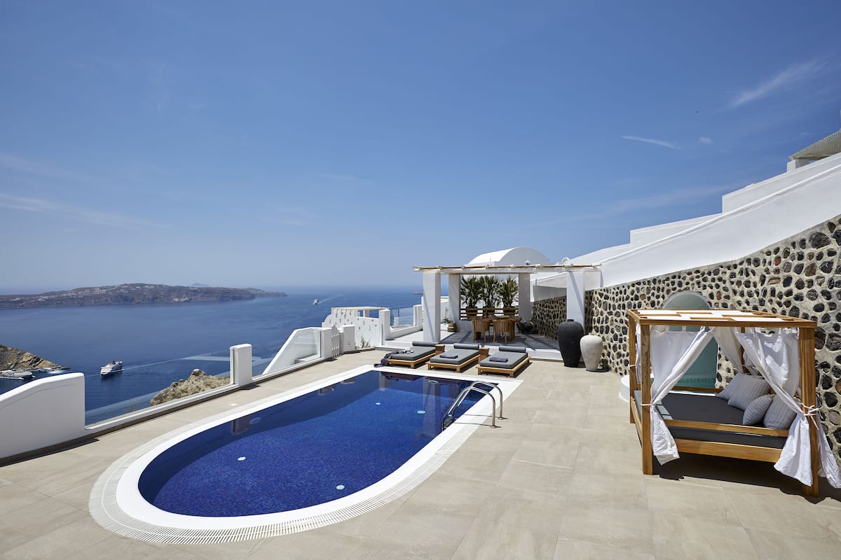 A pool with a view of the sea, a bed with a canopy, and a stone wall.