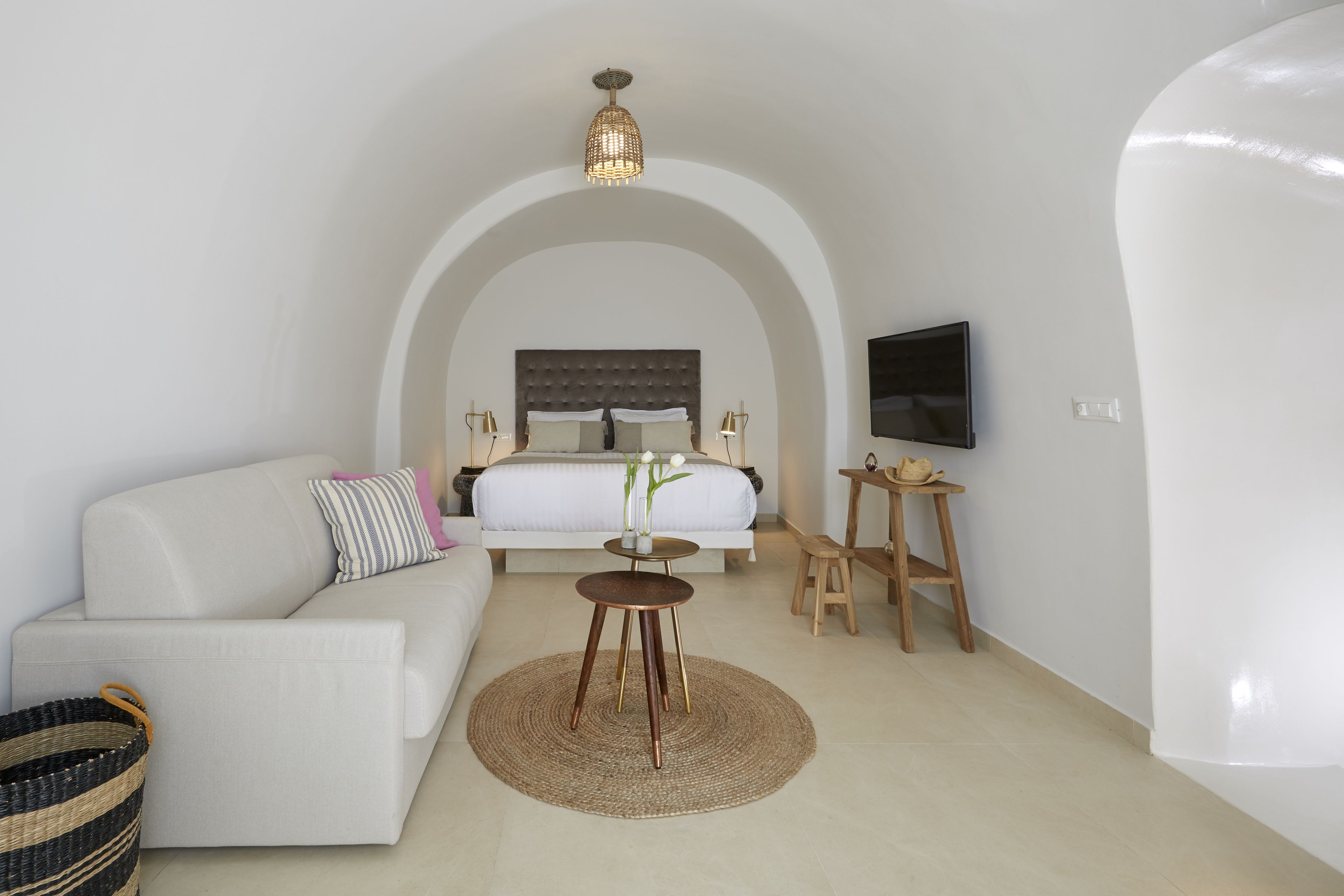 A modern hotel room with a large bed, a sofa, a small round table, a TV, and a unique arched ceiling.