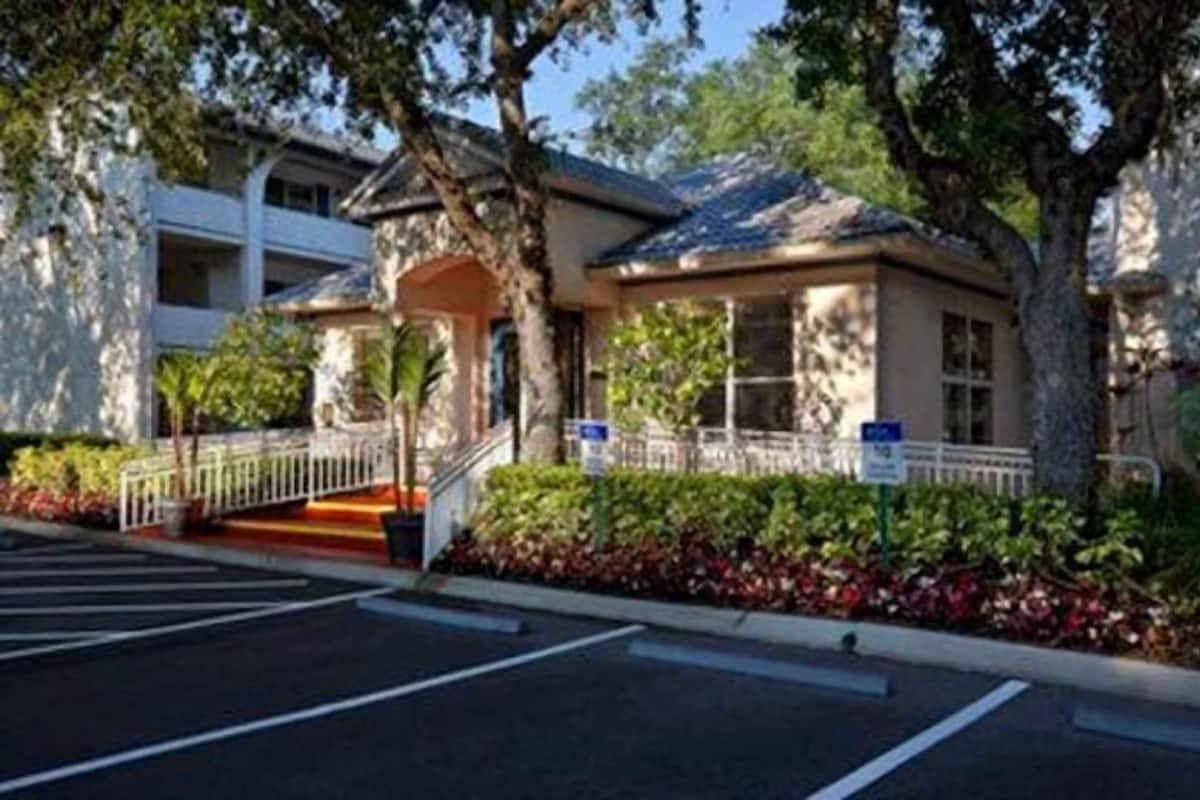 A building with a covered entrance, a parking lot, and a small garden area.